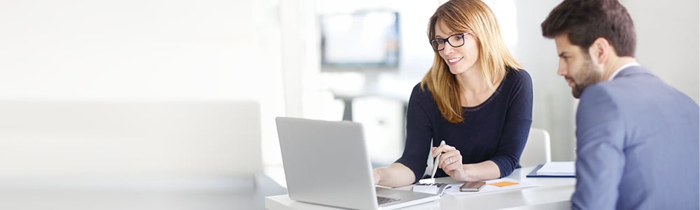 A woman and a man review business insurance documents on a laptop.